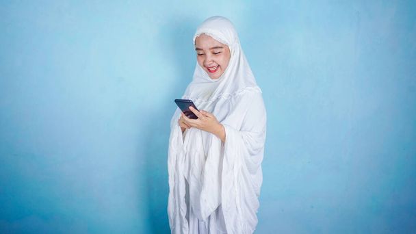 Çekici Asyalı Müslüman kadın sunuyor ve akıllı telefon tutuyor. boş kopya alanı mavi arkaplan üzerinde izole edildi - Fotoğraf, Görsel