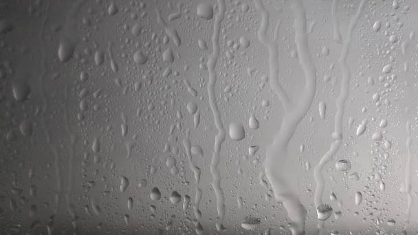 Regendruppels water stromen door het glas bij regenachtig weer op een grijze wazige achtergrond. Textuur en effect van regen op het raam - Video