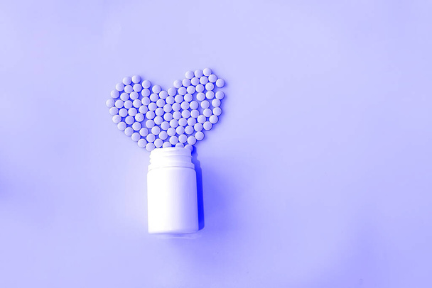 molte piccole pillole rovesciate da un barattolo bianco su uno sfondo viola a forma di sentire - Foto, immagini