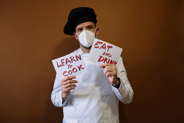 Chef hombre sosteniendo un cartel que dice Comer y beber, Él lleva una máscara en su cara - Foto, Imagen