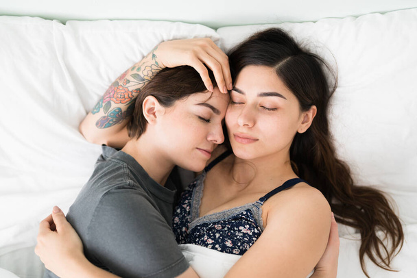 Atrakcyjna para lesbijek ściskająca się podczas snu w sypialni. Romantyczne młode dziewczyny relaks i patrząc spokojnie leżąc w łóżku  - Zdjęcie, obraz