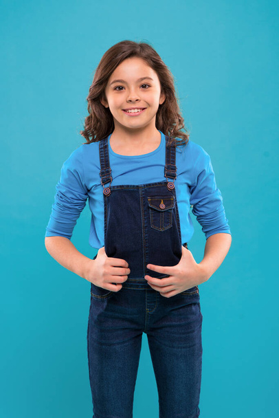Pure beauty. Little girl with long hair. Kid happy cute face with adorable curly hair stand over blue background. Beauty tips for tidy hair. Kid girl long healthy shiny hair wear casual clothes - Valokuva, kuva