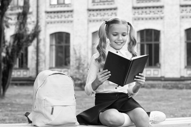 Schoolgirl cute child with backpack relax outdoors, reading book concept - Фото, зображення