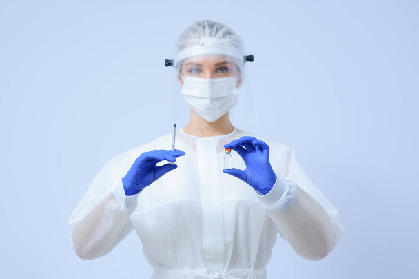 Γιατρός με ιατρικά γάντια και μάσκα κρατάει ένα εμβόλιο στα χέρια του. - Φωτογραφία, εικόνα