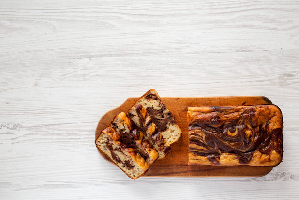 Homemade Chocolate Banana Bread on a rustic wooden board on a white wooden background, top view. Flat lay, overhead, from above. Space for text. - Foto, imagen