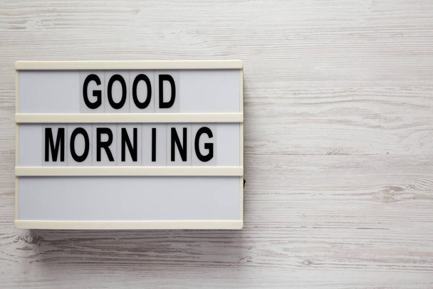 'Good morning' on a lightbox on a white wooden background, top view. Flat lay, overhead, from above. Space for text. - Фото, изображение