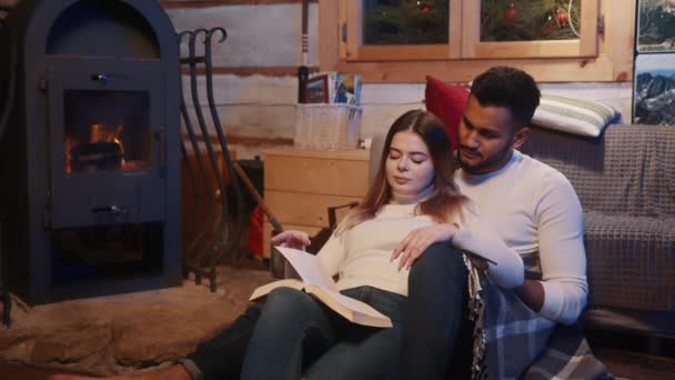 Glückliches junges Paar entspannt sich und liest gemeinsam Buch am Kamin. Winterurlaub, Weihnachten oder Valentinstag - Filmmaterial, Video