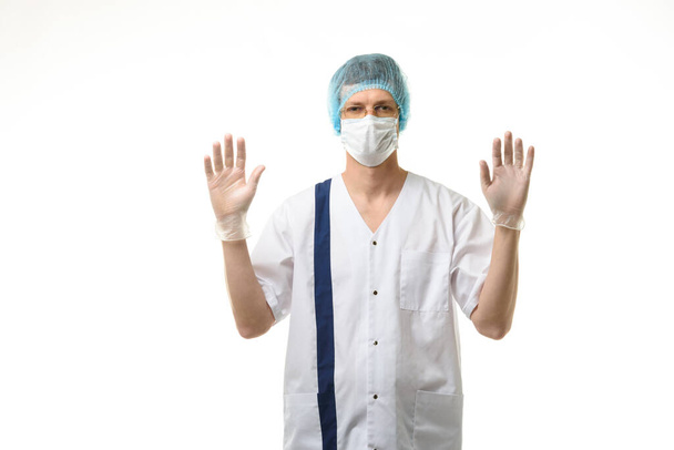 Un medico maschio sta in piedi con le mani alzate, i guanti indossati, una maschera e un cappello sulla testa - Foto, immagini