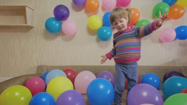 Cute little girl kicks colorful balloons with her feet. She laughs and rejoices - Footage, Video