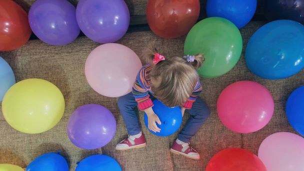 Mała, zabawna dziewczynka bawi się kolorowymi balonami. Strzał z góry - Zdjęcie, obraz
