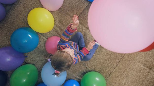 Little girl plays with balloons. Child throws pink ball up and rejoices - Фото, изображение