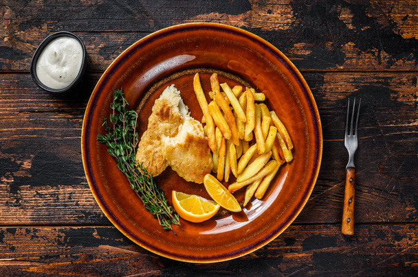 Fish and Chips british fast food with french fries and tartar sauce on a rustic plate. Dark wooden background. Top view - Foto, Bild