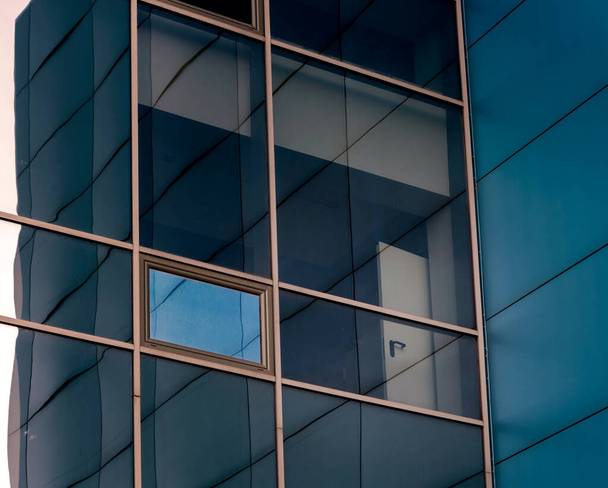 mirrored windows of the facade of an office building with blue panels and yellow window frames with a distorted reflection of the house - 写真・画像