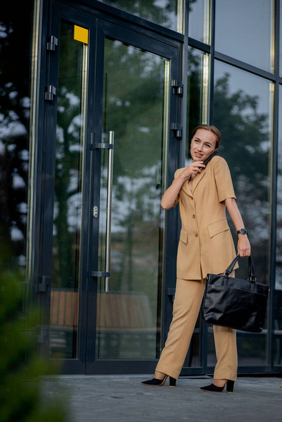 Adult Caucasian Confident Young Business Woman is Talking on Phone Outside near Modern Office Building. - 写真・画像