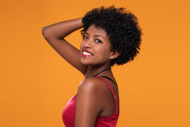 Beautiful smiling afro woman with glamour makeup looking at camera, posing on yellow studio background.  - Фото, изображение