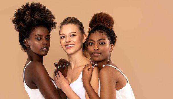 Three beautiful multi ethnic women posing together, looking at camera. Beauty portrait of two afro girl and one caucasian blonde. Skin care. Multiracial friendship. - Fotografie, Obrázek