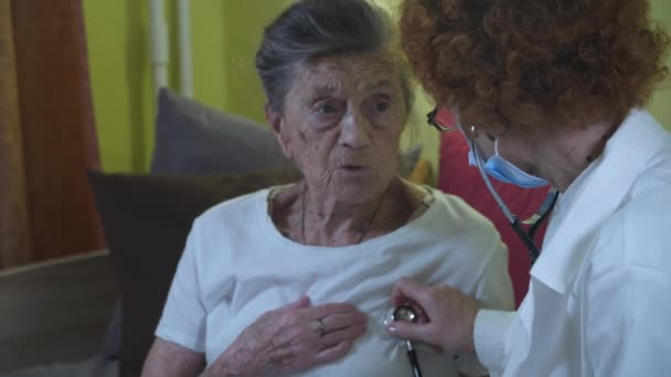 Пожилая белая женщина-врач слушает дыхание пожилого пациента, медицинское обследование стетоскопом, проверяет сердце и легкие пожилой женщины в доме престарелых. Инфекции, заболевания - Кадры, видео