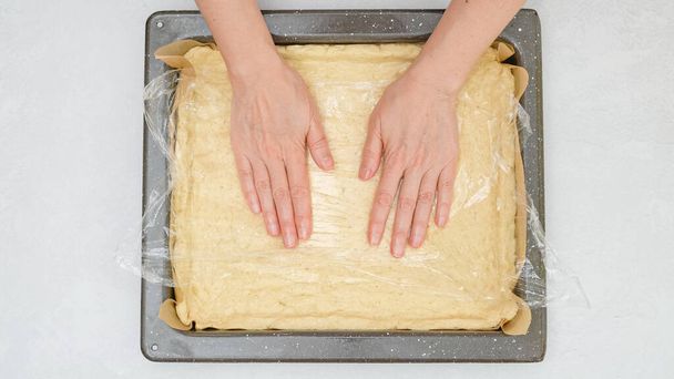 Las manos de la mujer colocando masa de pizza en la bandeja para hornear, vista de cerca desde arriba. - Foto, Imagen