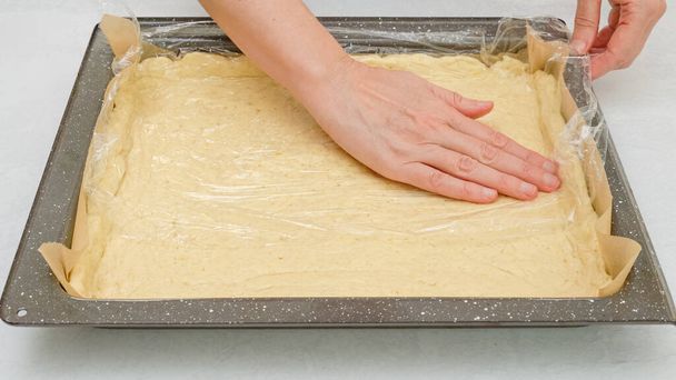 Za pomocą plastikowego owijania szefa kuchni rozwikłać ciasto pizzy na patelni. Zbliżenie krok po kroku pizzy domowej roboty przepis - Zdjęcie, obraz