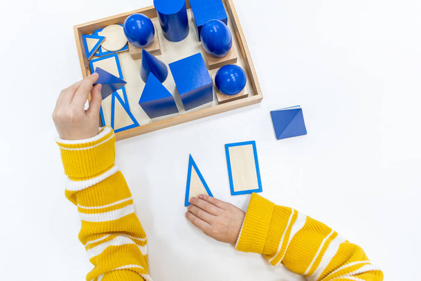 Top view of girls hand is playing and sorting a puzzle of colored wooden geometric shapes in montessori school. Concept of using a mathematical geometry learning resources for children education. - Foto, Imagem