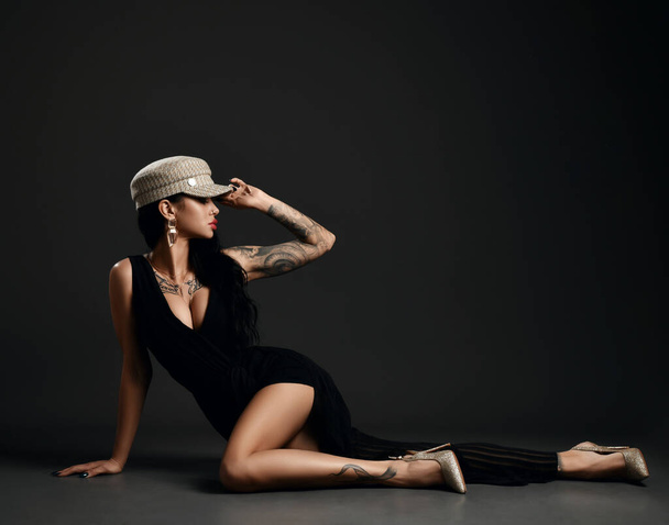 Gorgeous woman with tattoo on body and arms wearing pinstripe suit with deep neckline and naked leg is lying on floor - Foto, Imagem