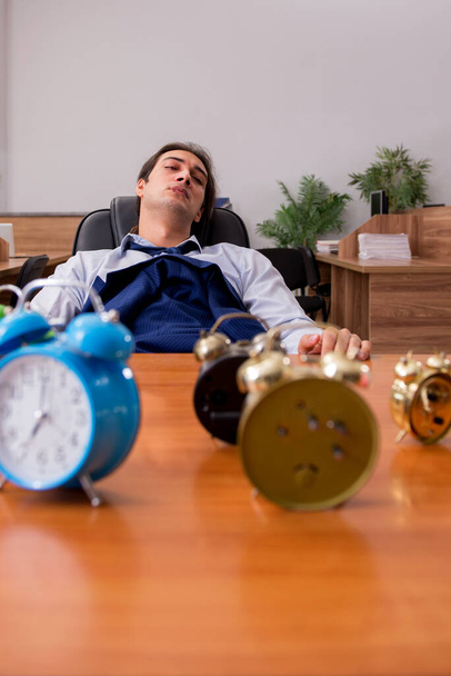 Νεαρός άνδρας εργαζόμενος κοιμάται στο γραφείο στη διαχείριση του χρόνου - Φωτογραφία, εικόνα