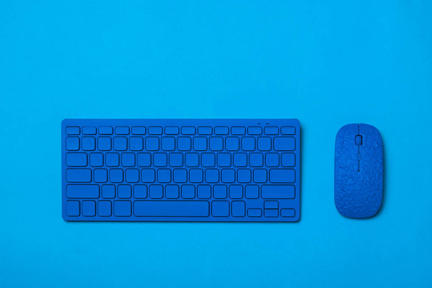 青い背景に青いワイヤレスキーボードとマウス。オフィスアクセサリーのモノクローム画像. - 写真・画像