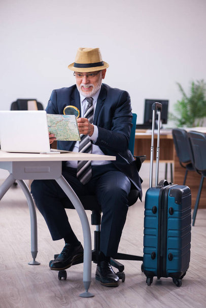 Old male employee preparing for travel in the office - Photo, image