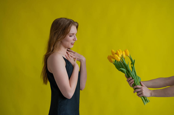 Caucasian woman accepts tulips as a gift on yellow background. - Foto, immagini