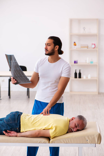 Old male patient visiting young male doctor chiropractor - Foto, Imagem
