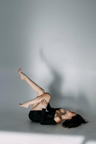 Model tests of a girl on a white cyclorama. A young brunette in a black short dress poses and lies on the floor. - Фото, зображення