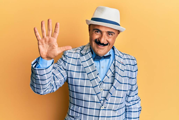 Homme mûr du Moyen-Orient avec moustache vêtue vintage et élégant style de mode montrant et pointant vers le haut avec les doigts numéro cinq tout en souriant confiant et heureux.  - Photo, image