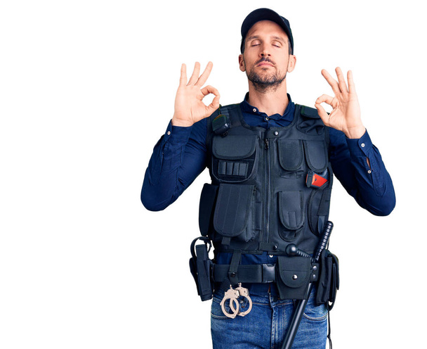 Ein junger gutaussehender Mann in Polizeiuniform entspannt und lächelnd mit geschlossenen Augen, der Meditationsgeste mit den Fingern macht. Yoga-Konzept.  - Foto, Bild