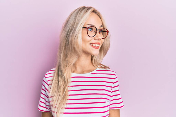 Beautiful caucasian blonde girl wearing casual clothes and glasses looking to side, relax profile pose with natural face and confident smile.  - Foto, Bild