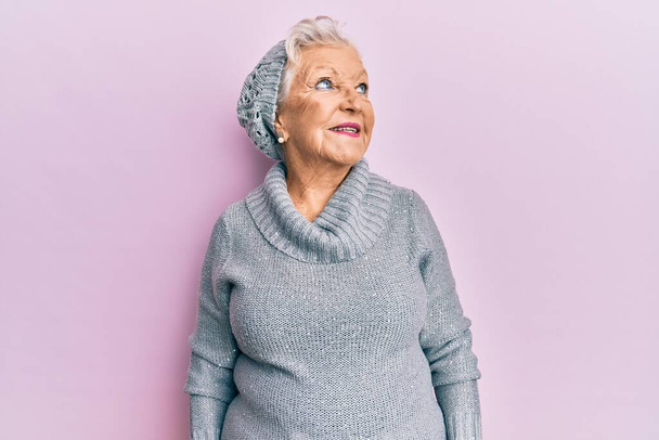 Senior grey-haired woman wearing wool sweater and winter hat looking away to side with smile on face, natural expression. laughing confident.  - Foto, Imagen