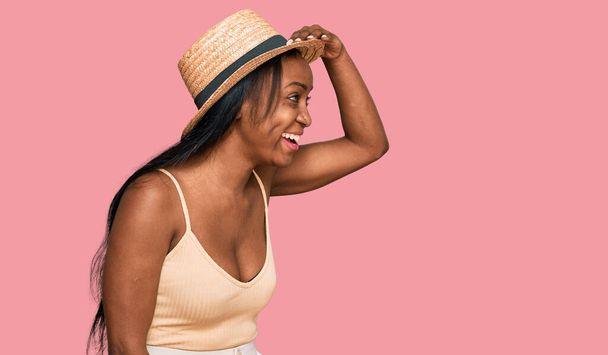 Young black woman wearing summer hat very happy and smiling looking far away with hand over head. searching concept.  - Photo, Image