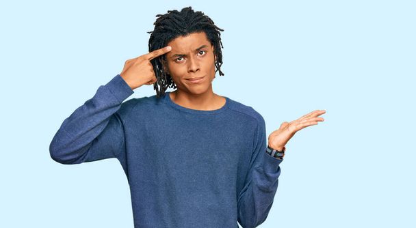 Молодий афроамериканець у повсякденному зимовому светрі збентежений і роздратований відкритою пальмою, що показує простір для копіювання і вказує пальцем на лоб. Подумайте про це..  - Фото, зображення