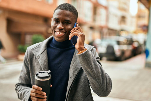 Młody Afroamerykanin rozmawiający przez smartfona pijący kawę w mieście - Zdjęcie, obraz