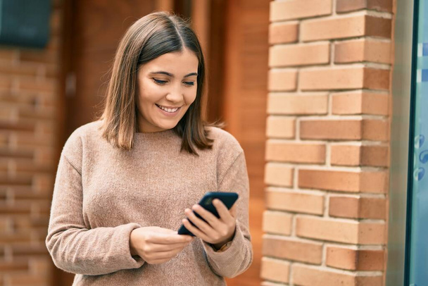 Молода іспаномовна жінка посміхається щасливим використанням смартфона в місті
. - Фото, зображення