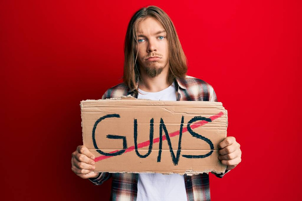 Handsome caucasian man with long hair holding no guns warning banner depressed and worry for distress, crying angry and afraid. sad expression.  - Photo, Image