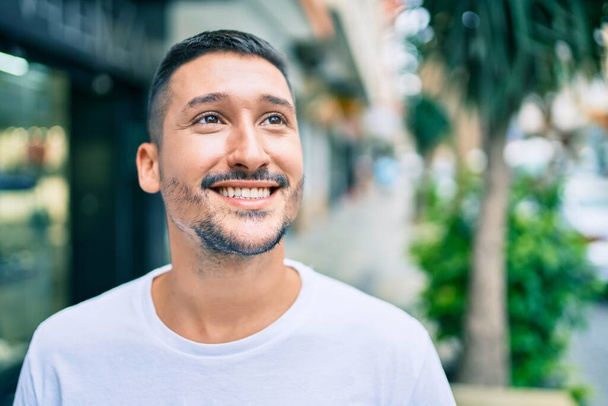 Mladý hispánec se šťastně usmívá při procházce ulicí města. - Fotografie, Obrázek