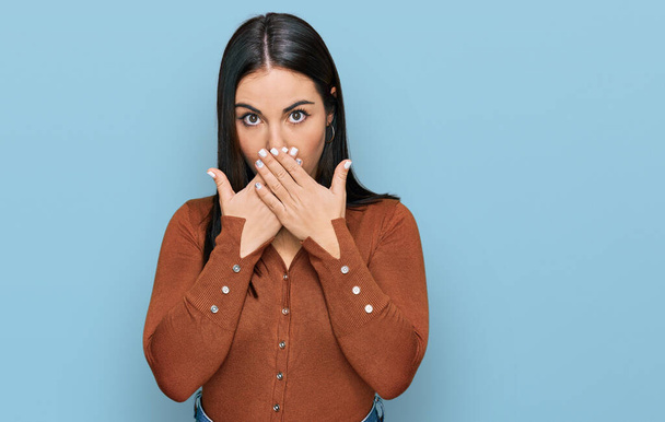 Jonge Latijns-Amerikaanse vrouw in casual kleding geschokt bedekken mond met handen voor fout. geheim concept.  - Foto, afbeelding