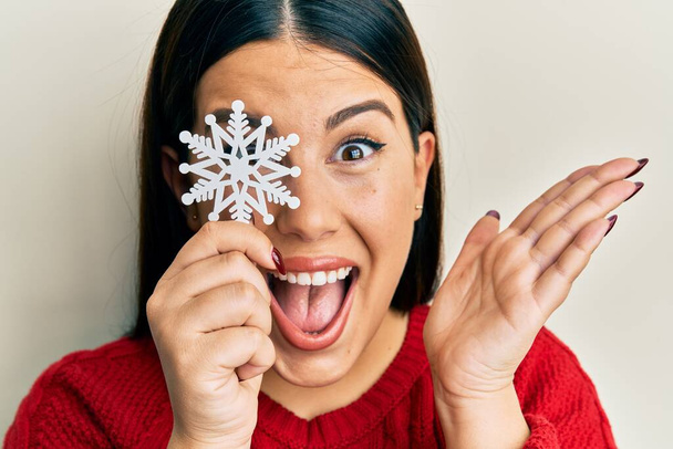 Bella donna bruna che tiene il fiocco di neve sopra l'occhio celebrando il successo con sorriso felice e espressione del vincitore con la mano sollevata  - Foto, immagini