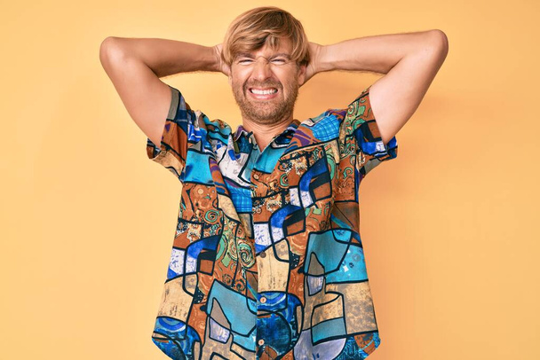 Young blond man wearing summer shirt relaxing and stretching, arms and hands behind head and neck smiling happy  - Fotoğraf, Görsel