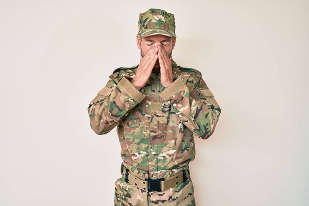 Jonge blanke man draagt camouflage legeruniform wrijvende ogen voor vermoeidheid en hoofdpijn, slaperige en vermoeide uitdrukking. gezichtsproblemen  - Foto, afbeelding