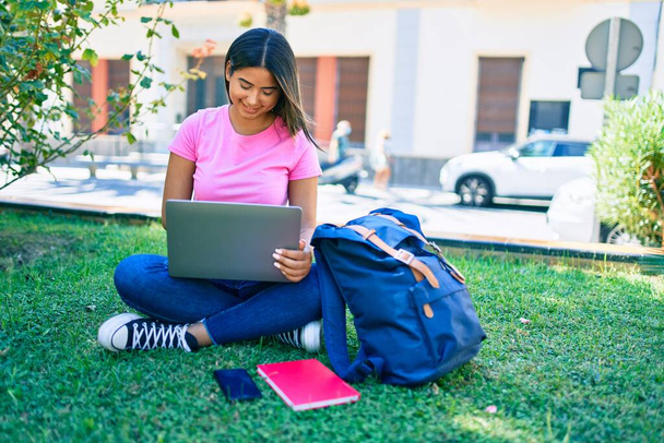 Joven estudiante latina sonriendo feliz usando laptop en campus universitario - Foto, imagen