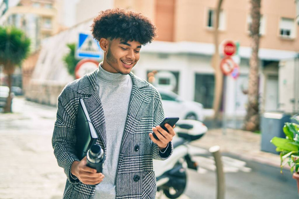 Junger afrikanisch-amerikanischer Geschäftsmann hält mit Smartphone Wasserflasche in der Stadt. - Foto, Bild