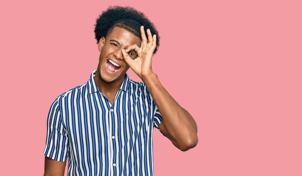 afro americano uomo con afro capelli indossare casual vestiti sorridente felice fare ok segno con mano su occhio guardando attraverso le dita  - Foto, immagini