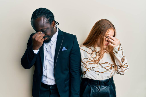 Young interracial couple wearing business and elegant clothes tired rubbing nose and eyes feeling fatigue and headache. stress and frustration concept.  - Photo, Image