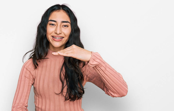 Spanyol tinédzser lány fogszabályzó visel alkalmi ruhát gesztikuláló kezek mutató nagy és nagy méretű jel, intézkedés szimbólum. mosolyogva néz a kamerába. mérési koncepció.  - Fotó, kép